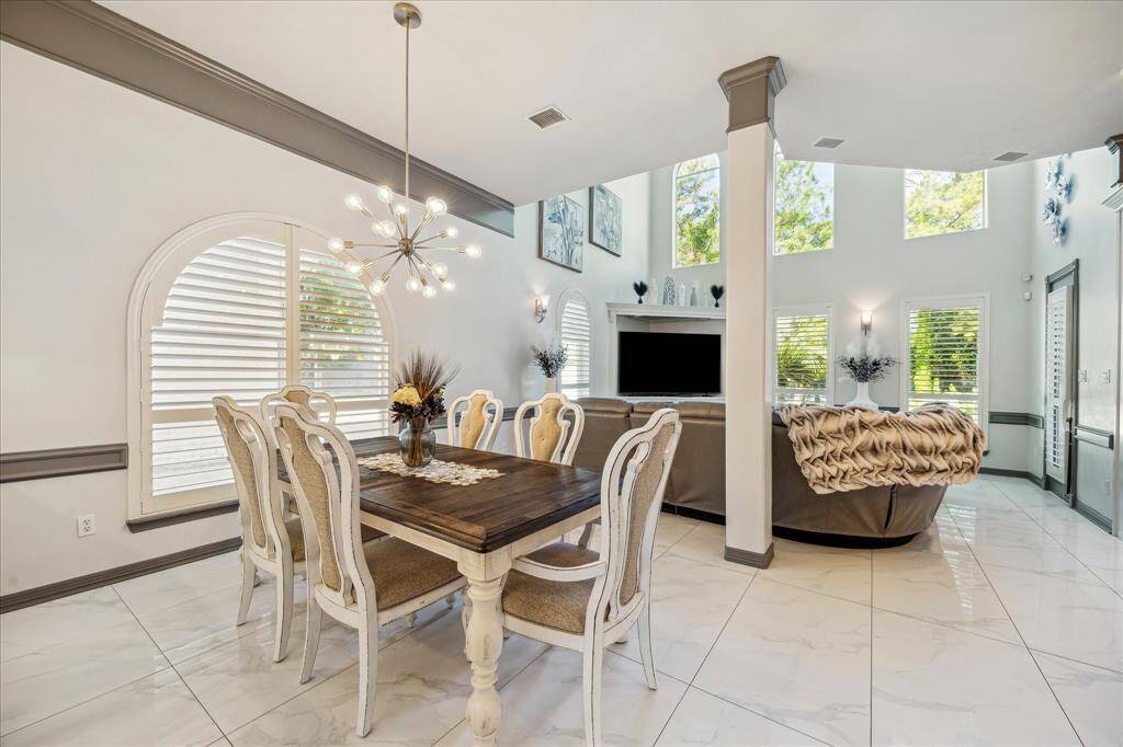 This spacious living and dining area features high ceilings, large windows with abundant natural light, and elegant tile flooring. The open layout includes a cozy family room that is open to the kitchen and breakfast area.