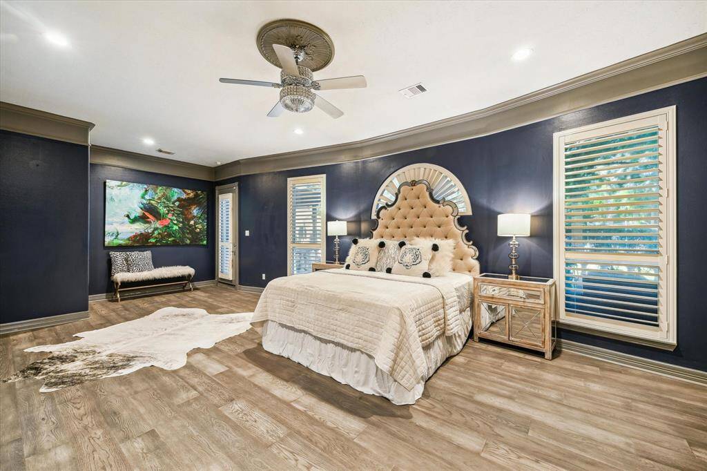 This spacious primary bedroom features elegant navy walls and wood flooring. The room is well-lit with large windows creating a cozy yet sophisticated atmosphere.