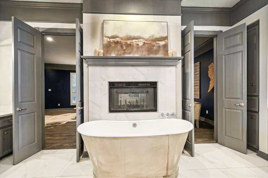 This elegant bathroom features a freestanding tub in front of a dual-sided fireplace, creating a luxurious and cozy atmosphere. The surrounding tiles and neutral palette enhance the sophisticated design.