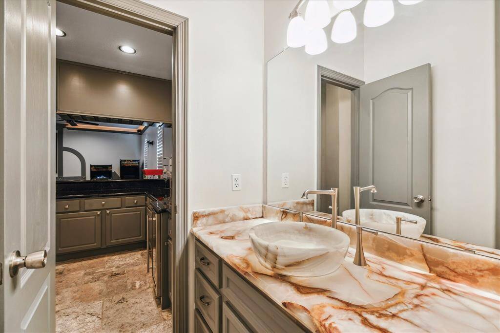 This photo shows a modern wet bar area with sleek black granite countertops, under-counter sink, ample cabinetry, and a compact refrigerator open to the media room.