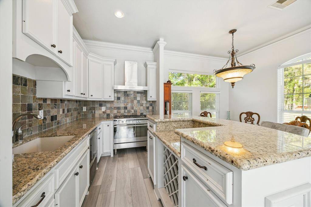 This kitchen features elegant white cabinetry, a stainless steel refrigerator, and a tiled backsplash. The granite countertops include a breakfast bar with plush seating, creating a cozy and functional space.