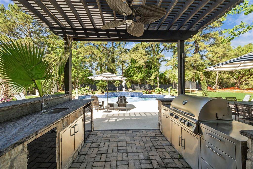 This backyard features a spacious patio with outdoor seating and umbrellas, a swimming pool with a spa, and lush landscaping with mature trees. Ideal for relaxation and entertaining.