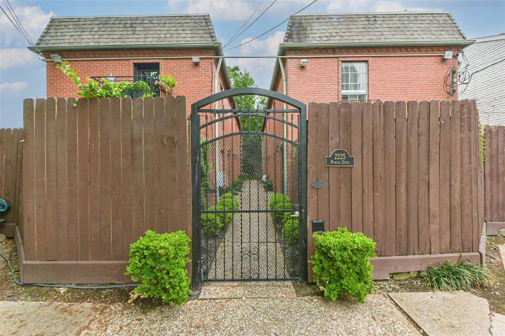 This photo shows a charming brick property with a gated entrance and wooden fencing. The pathway is lined with greenery, adding a touch of nature and privacy to the home.
