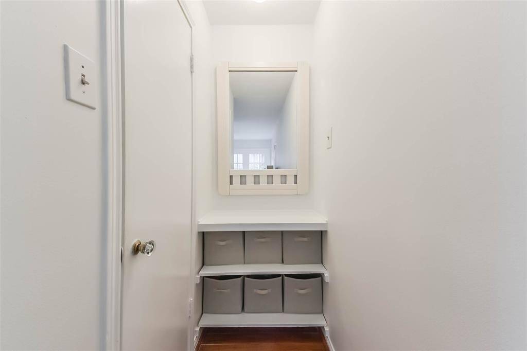 This photo shows a small, well-lit hallway nook with a white wall-mounted mirror above a shelf. Beneath the shelf are storage bins, offering practical organization. The space is simple and functional.
