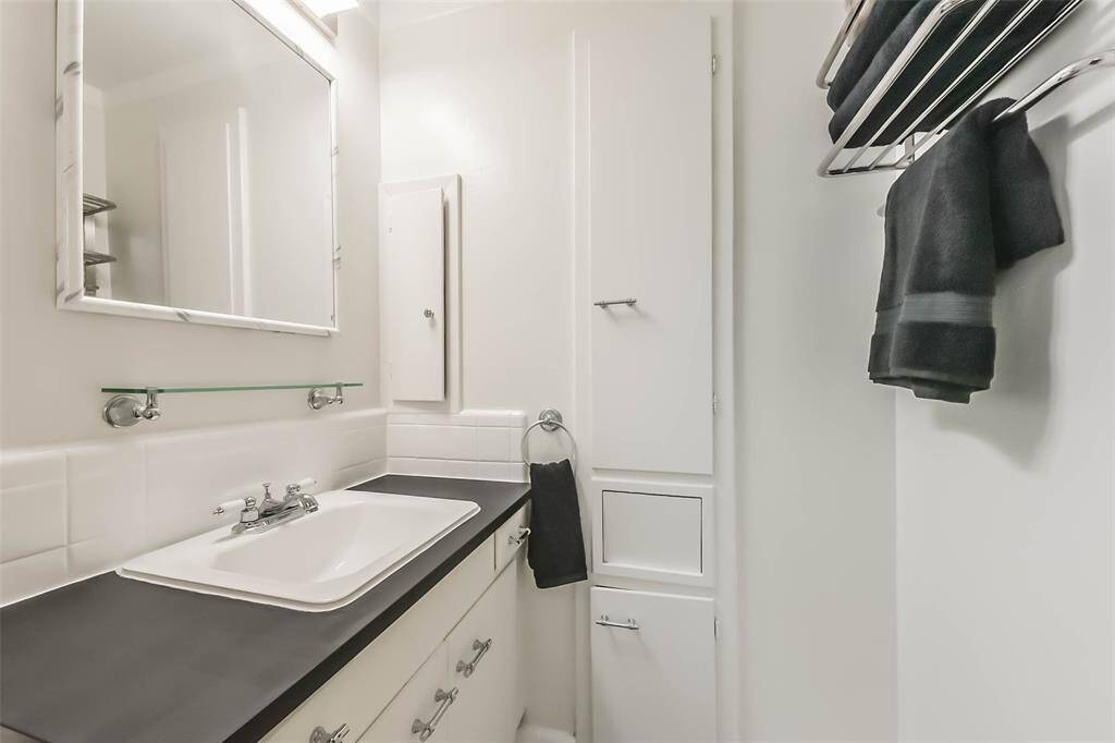 This photo showcases a compact, modern bathroom with a sleek black countertop and white cabinetry. It features a large mirror, a single basin sink, and a towel rack with neatly folded towels, providing a clean and functional space.