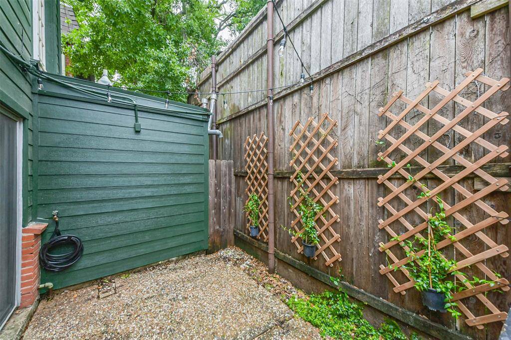 This photo shows a small, enclosed outdoor area with a green exterior wall and wooden fence. There are trellises with plants along the fence, and the ground is covered with gravel. It's a cozy space for gardening or relaxing.