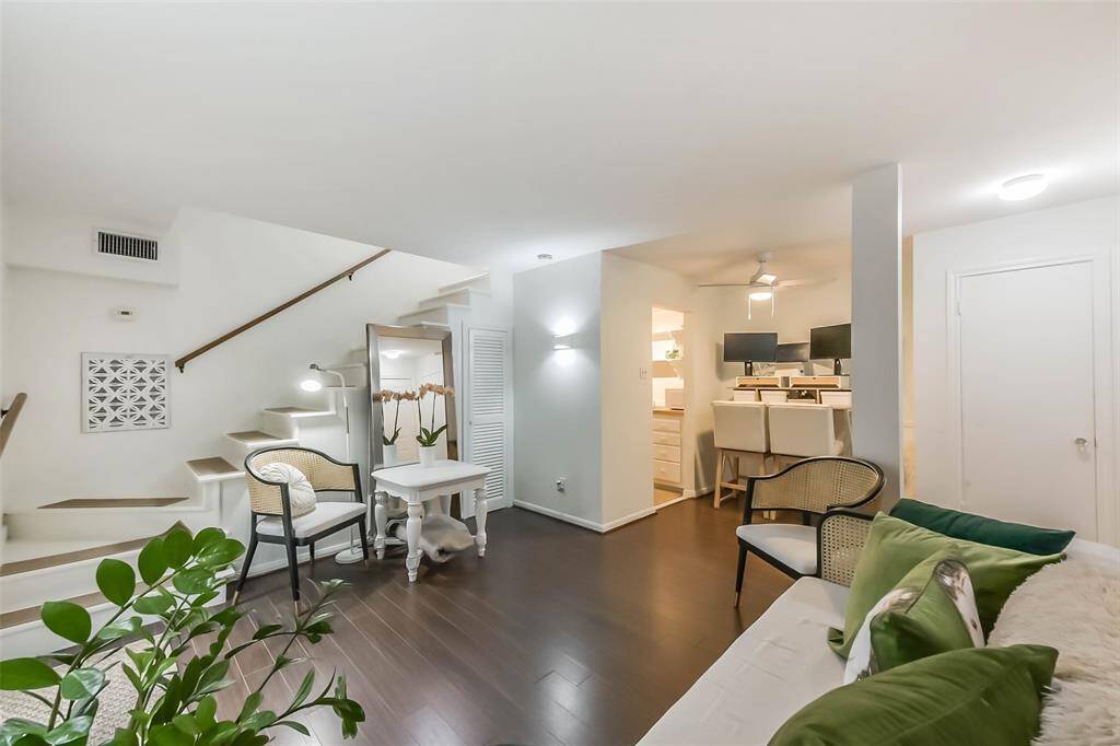 This photo showcases a cozy, open-plan living area with dark wood flooring and modern decor. The space is bright with white walls, featuring a staircase leading to an upper level. A small dining area with a breakfast bar is visible, and there's ample natural light, creating an inviting atmosphere.