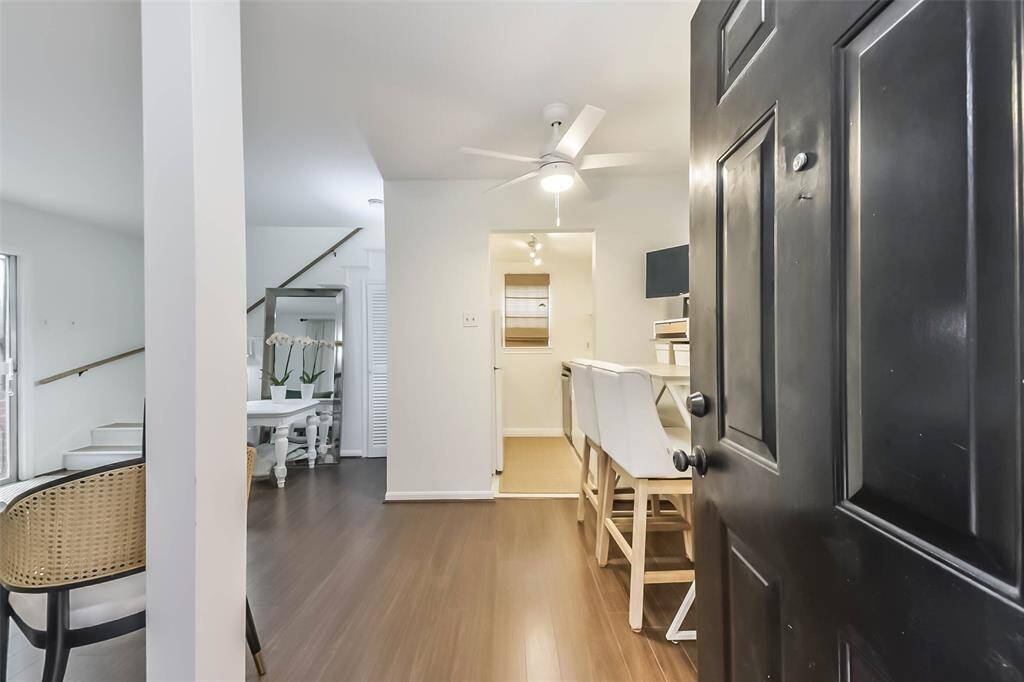 Welcome to this inviting home featuring an open-concept layout with sleek hardwood floors. A modern kitchen with a breakfast bar is visible from the entrance, complemented by a cozy dining area. The space is bright and airy, enhanced by a ceiling fan and natural light, perfect for comfortable living.