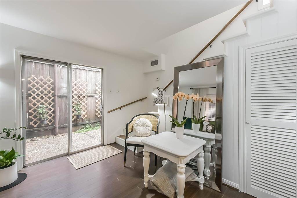 Bright, cozy room with hardwood floors, featuring a large mirror, small desk, and chair. Sliding glass doors lead to a fenced patio area, adding natural light. Perfect for a home office or reading nook.