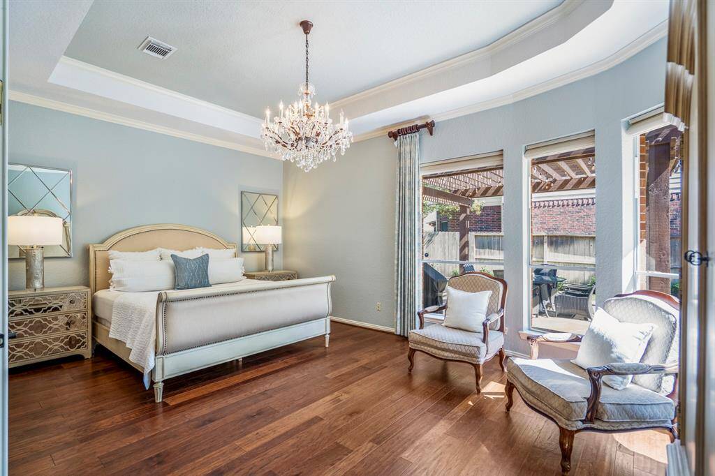 Luxurious downstairs primary bedroom with elegant chandelier, abundant natural light, and garden views.