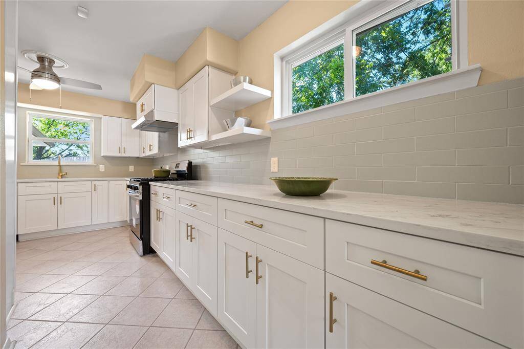 Modern kitchen featuring white cabinetry, stainless steel appliances, and a ceiling fan. It has ample counter space, a gas stove, and a large window for natural light.