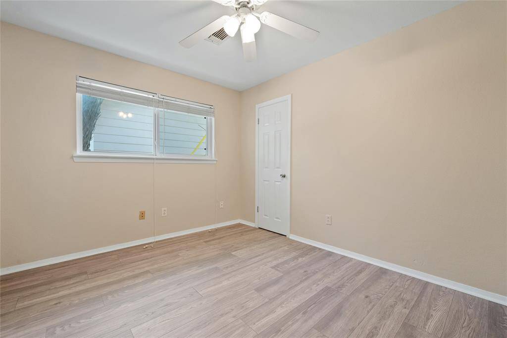 Secondary bedroom features neutral walls, wood-look flooring, a ceiling fan with lights, and a window with blinds, providing a bright and airy feel.