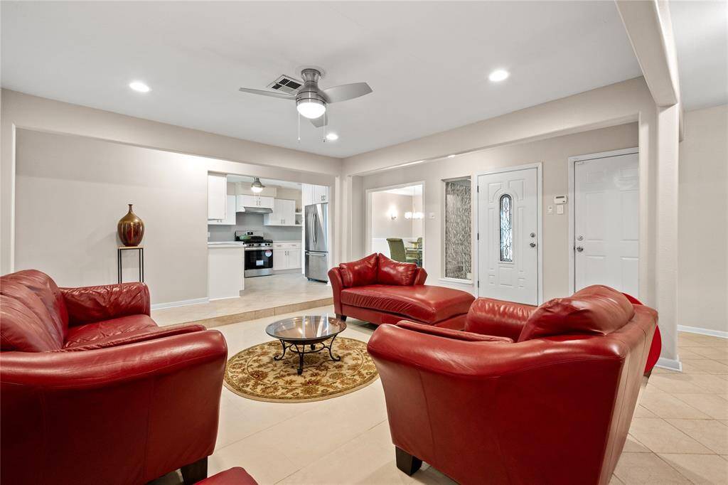 Living room, featuring sleek tile floors, modern lighting, and neutral walls. The space offers a ceiling fan and seamless access to adjoining rooms, perfect for relaxation and entertaining.