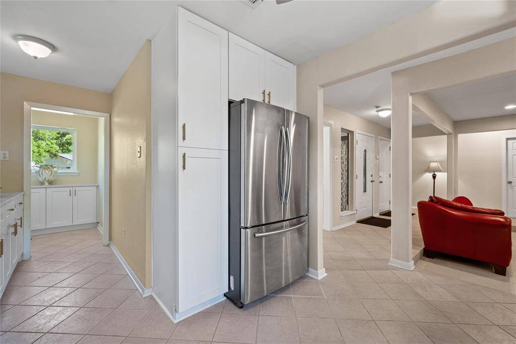 Modern kitchen with white cabinetry, stainless steel appliances, and a ceiling fan. Features tile flooring, a double-door fridge, and a sleek backsplash. Bright and spacious layout. Refrigerator included!