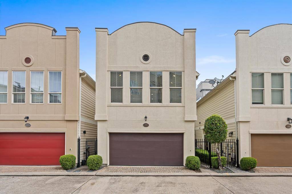 This photo shows a modern townhouse with a clean, neutral facade and a two-car garage. It's part of a row of similar homes (this is one of two without shared walls) offering a cohesive and stylish exterior with well-maintained landscaping and a gated entrance.