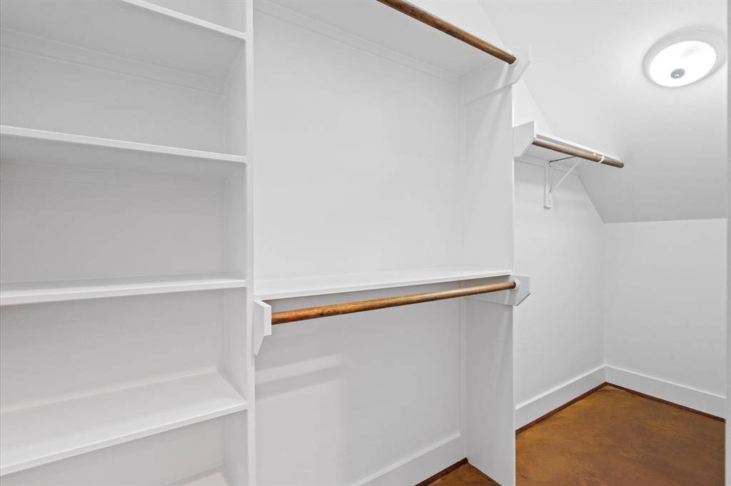 Spacious walk-in closet featuring multiple wooden hanging rods and built-in shelves, offering ample storage in a bright, white space.