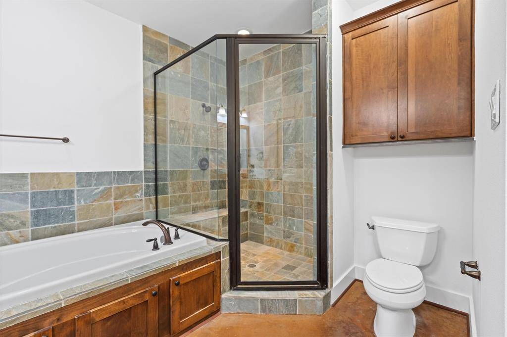 This bathroom features a spacious walk-in shower with glass doors and slate tile, a large bathtub with matching tile surround, a wooden cabinet for storage, and a sleek, modern toilet. The combination of natural tones and wood accents creates a warm and inviting atmosphere.