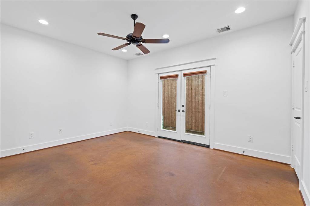 Bright primary room with white walls, recessed lighting, and a ceiling fan. Features double glass doors leading outside and a polished concrete floor, offering a modern and open feel.