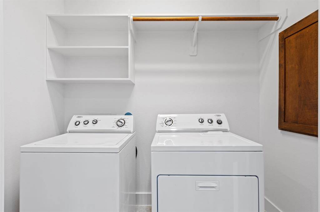 This photo shows a laundry room equipped with a washer and dryer. It features open shelving for storage and a wooden rod for hanging clothes, offering functional and organized space.