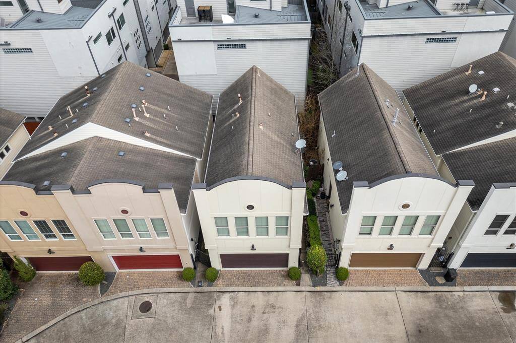 This aerial view shows a row of modern townhouses with uniform architecture, featuring two-story facades, large windows, and attached garages. The homes are closely spaced, with tidy landscaping and brick driveways, suggesting a well-maintained community.