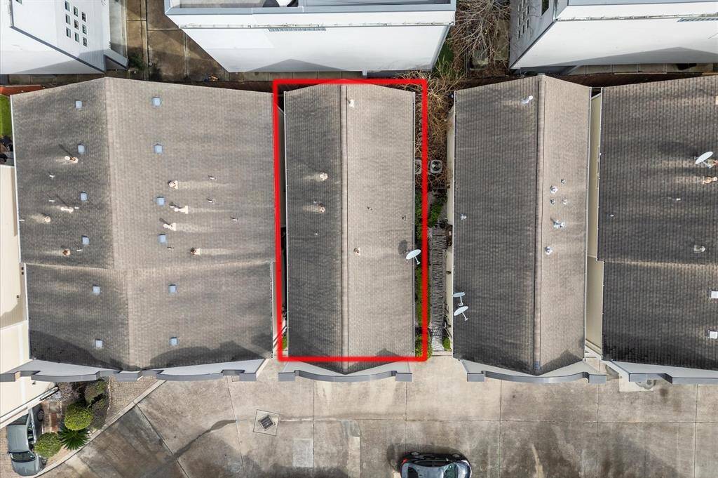 This aerial photo shows a townhouse (outlined in red), situated between two similar buildings. The property has a gray rooftop and appears to be part of a closely-knit residential complex. There's a paved area in front for parking.