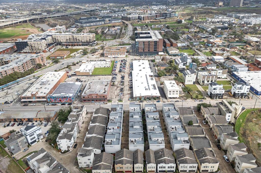 The photo showcases a vibrant urban neighborhood with modern townhouses and apartment buildings. It features a mix of residential and commercial areas, with green spaces and convenient access to major roads. The setting suggests a thriving community with diverse amenities.