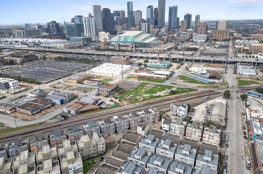 This aerial photo showcases a vibrant urban area with modern townhouses in the foreground and a bustling city skyline in the background. The neighborhood has a mix of residential and commercial buildings, with proximity to major roadways and public transportation, providing convenient access to city amenities.
