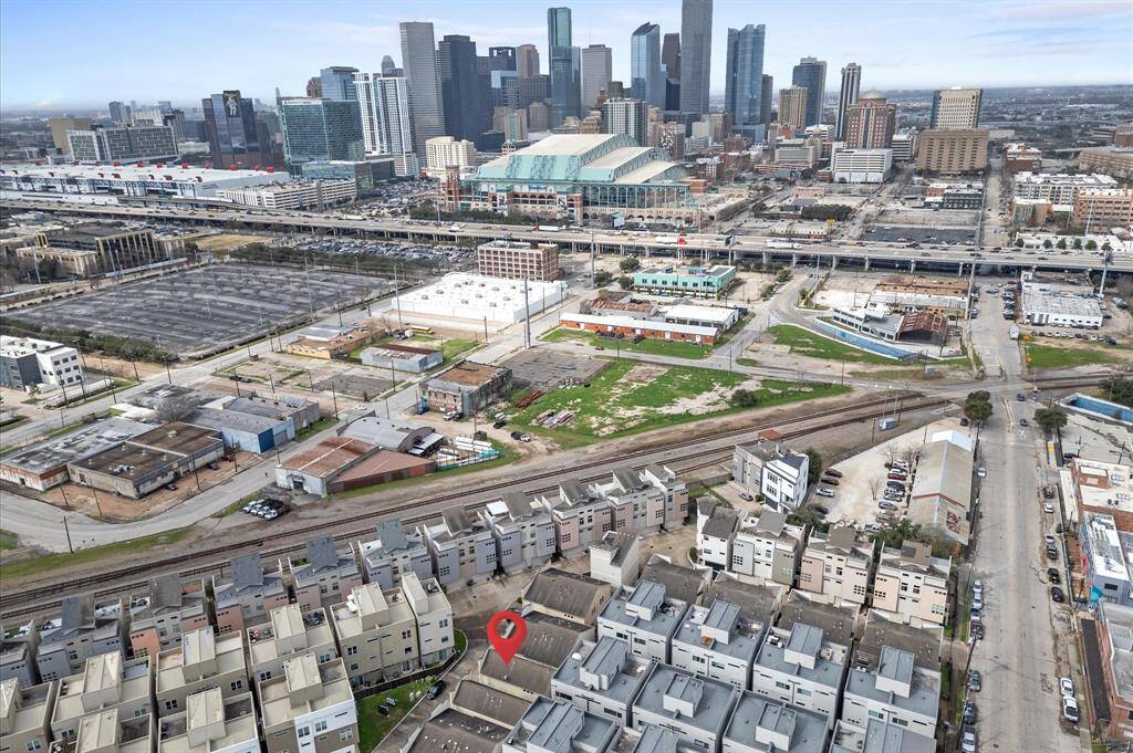 The photo showcases a residential area with modern townhouses, located near a vibrant urban center. The skyline features tall buildings, indicating proximity to a bustling downtown. Key infrastructure such as major roads and rail lines are visible, suggesting good connectivity. The area has a mix of residential and commercial spaces, offering convenience and accessibility.