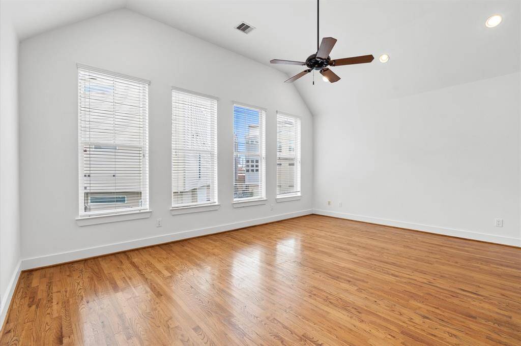 This spacious family room features high ceilings, hardwood floors, and ample natural light from large windows with blinds.  A ceiling fan adds comfort and style.
