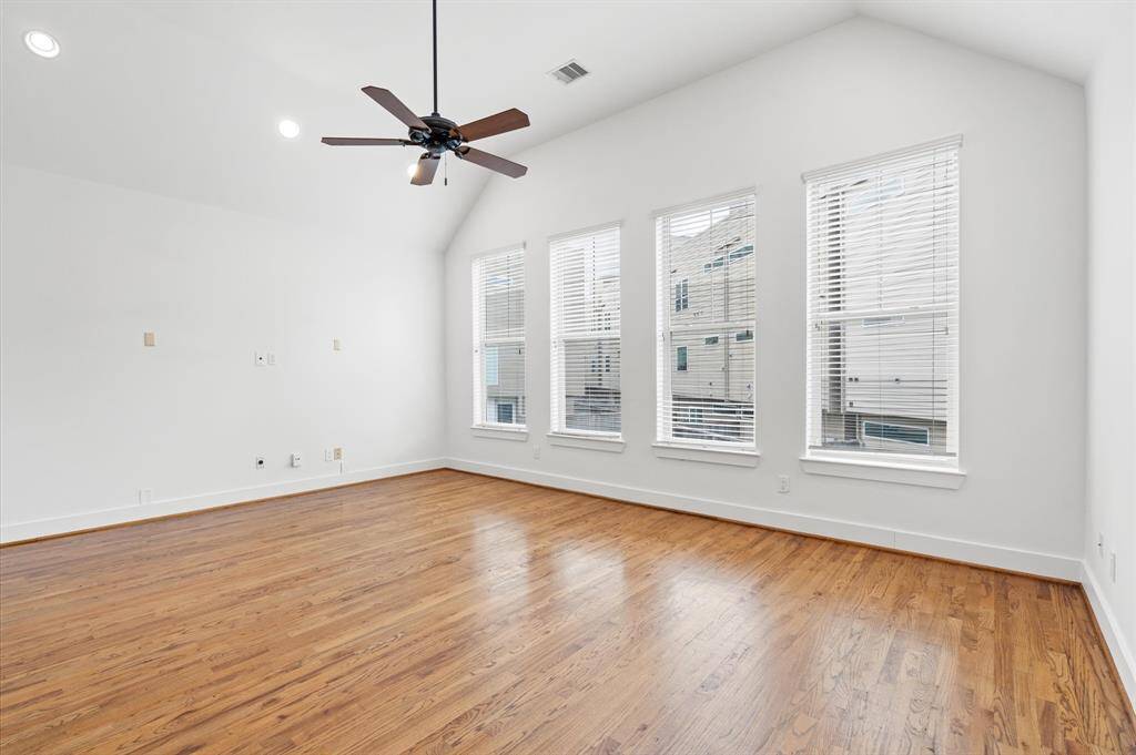 This spacious family room features hardwood flooring, large windows with blinds for ample natural light, and a ceiling fan for comfort.  The neutral walls and high ceiling create an open, airy feel, ideal for versatile styling.