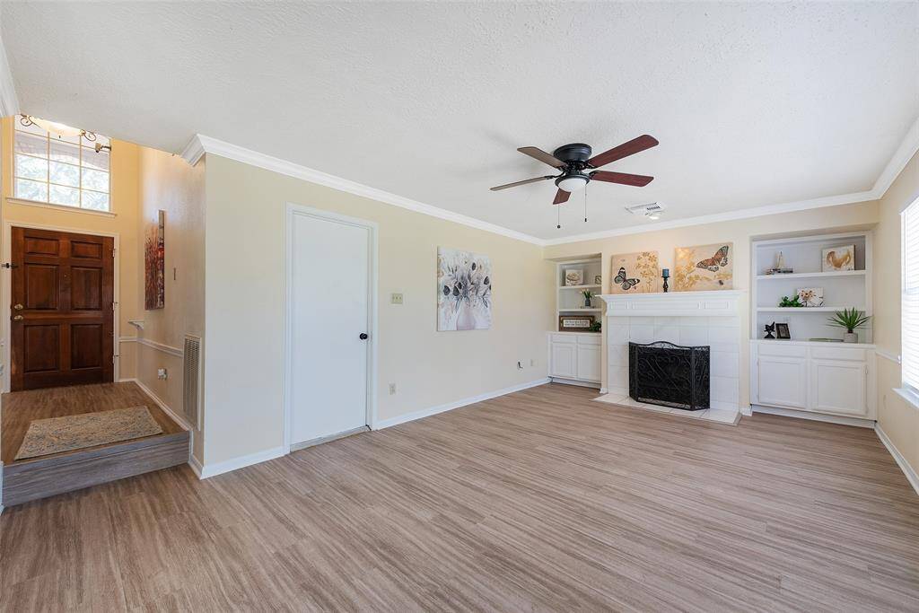 The family room with tile framed gas fireplace & built-ins on each side. A recessed light highlights the fireplace mantle. The room also has crown molding & a lighted ceiling fan.