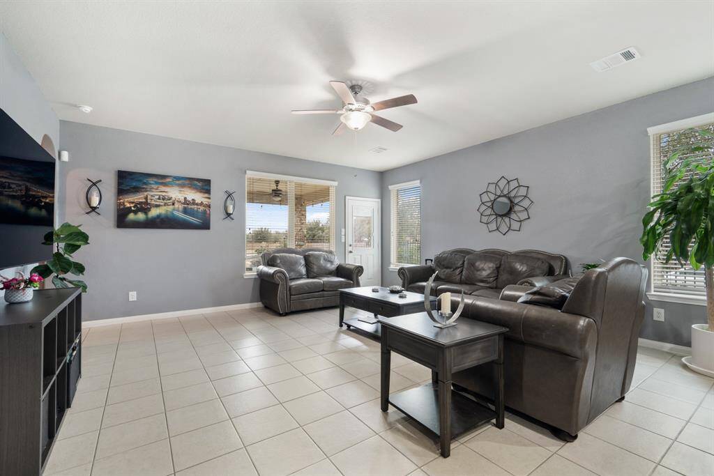 This stunning living area features tile floors, a ceiling fan, and windows with privacy blinds.