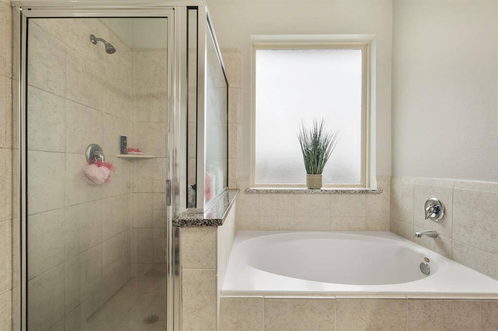 This incredible primary bathroom is complete with a large garden style tub, beautiful glass enclosed shower with a gorgeous tiling, and a large window with privacy glass providing natural light.