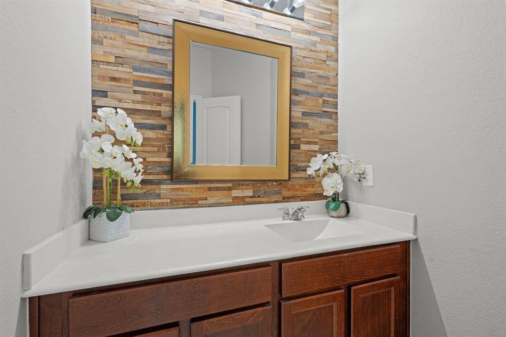 Secondary bathroom with granite countertops and backsplash, gorgeous wood grain accent wall, and wooden cabinetry.