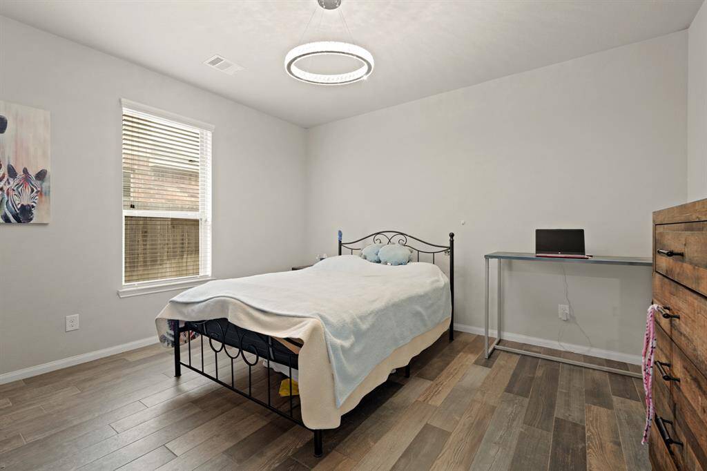 Secondary bedroom located on the first floor with engineered wood floors, and a window with privacy blinds.