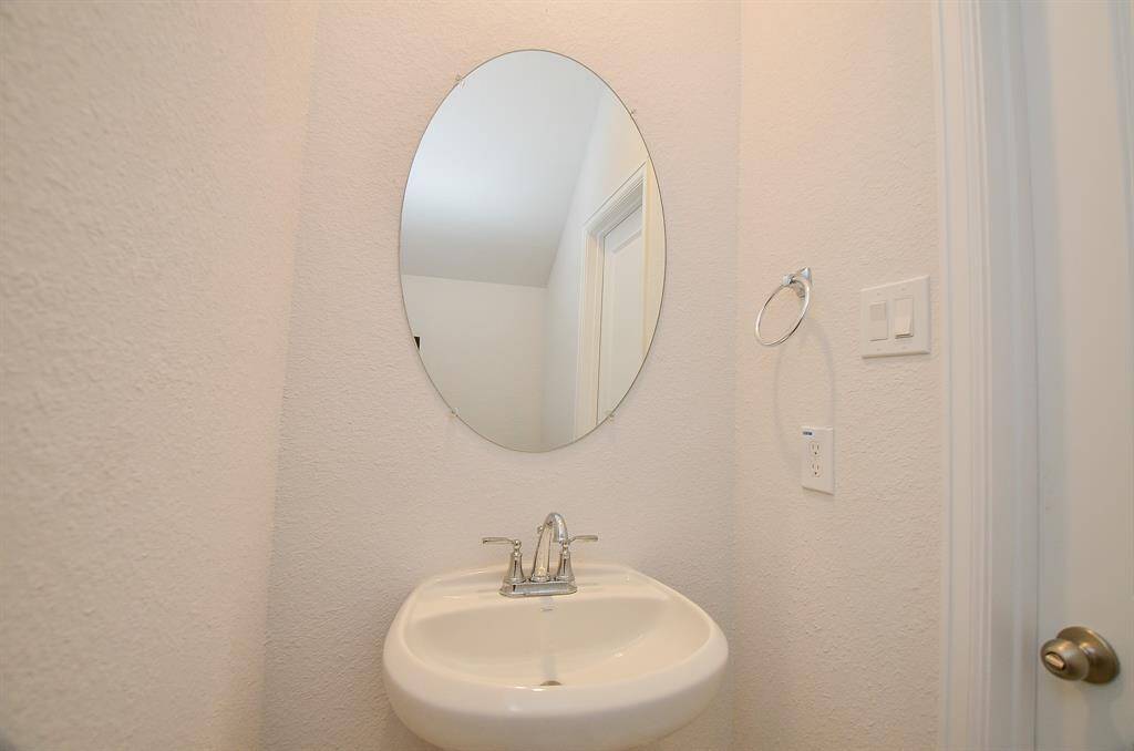 A small half-bathroom with a round mirror and pedestal sink.