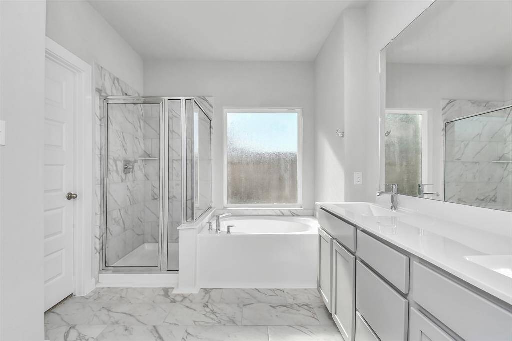 Escape to a spa-like oasis in this primary bathroom. Enjoy a walk-in shower with tile surround, a separate garden tub with custom detailing, and an elegant vanity featuring light countertops, modern hardware, and beautiful recessed lights. Experience luxury and relaxation in every detail. Sample photo of completed home with similar floor plan. Actual colors and selections may vary.