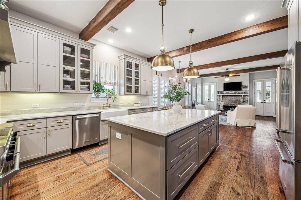CUSTOM PENDENTS LIGHT UP THE CARERRA MARBLE COUNTERTOPS OVER THE ISLANDCUSTOM-BUILT CABINETS INCLUDE AMPLE STORAGE AND ELECTRIC IN THE ISLAND APRON SINK OFFERS CUSTOM UN-LACQUERED BRASS FAUCET