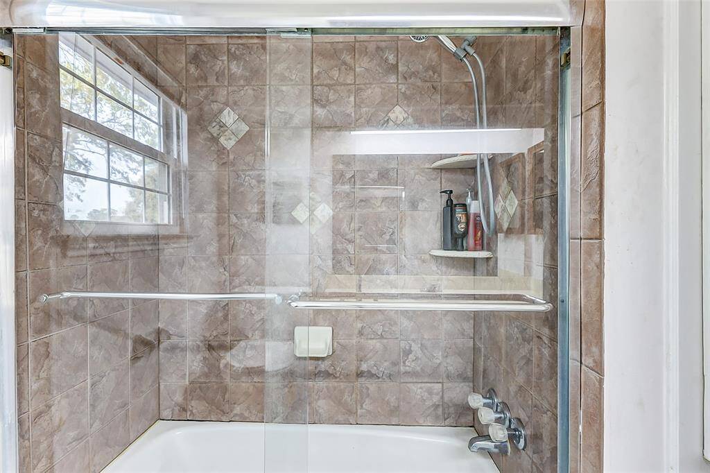 The tub/shower combination is enclosed by sliding glass doors and boasts a neutral tile surround that extends all the way to the ceiling, adding a touch of elegance and practicality.
