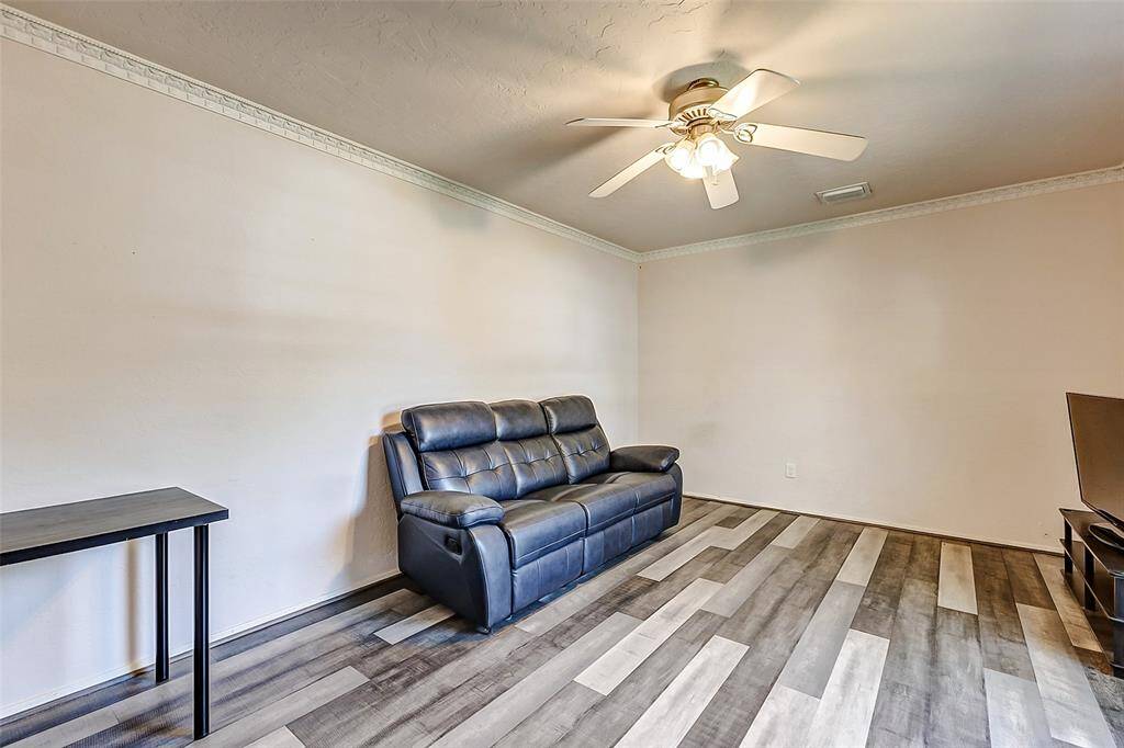 To the right of the entryway, the formal living room features updated flooring, neutral paint, and elegant crown molding, with a ceiling fan for added comfort.