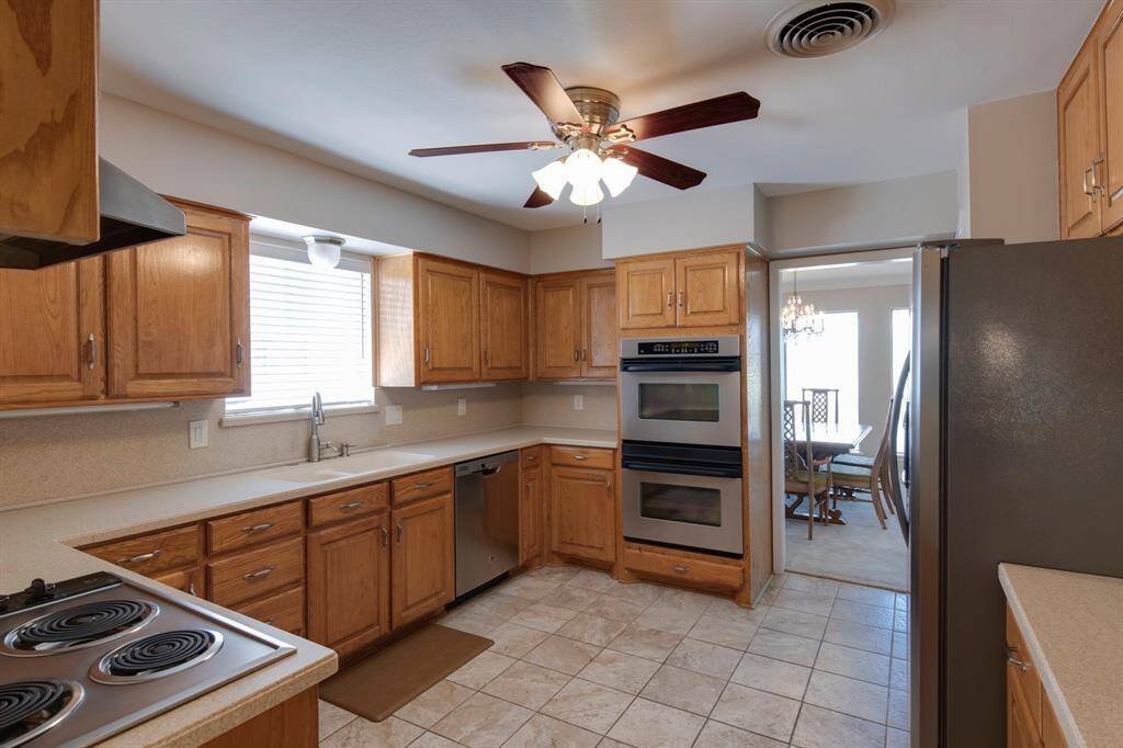 Kitchen has double wall ovens, tile floor, ceiling fan and refrigerator.
