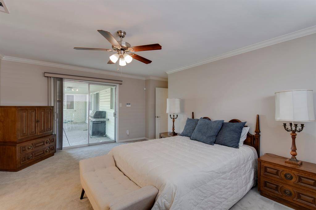 Primary bedroom has crown molding, carpet, ceiling fan and sliding glass doors that lead to the covered patio.