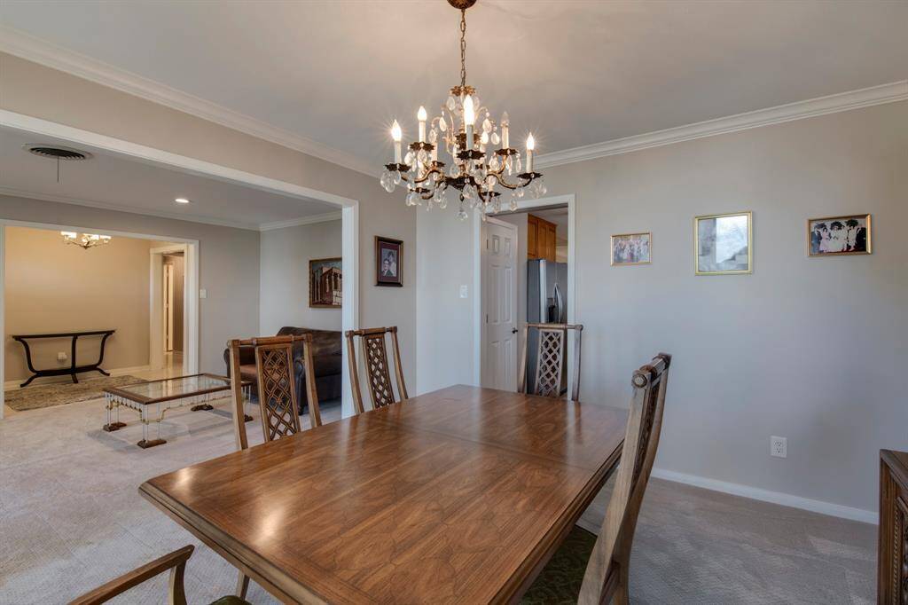 Formal dining room off the kitchen has crown molding, chandelier and carpet.
