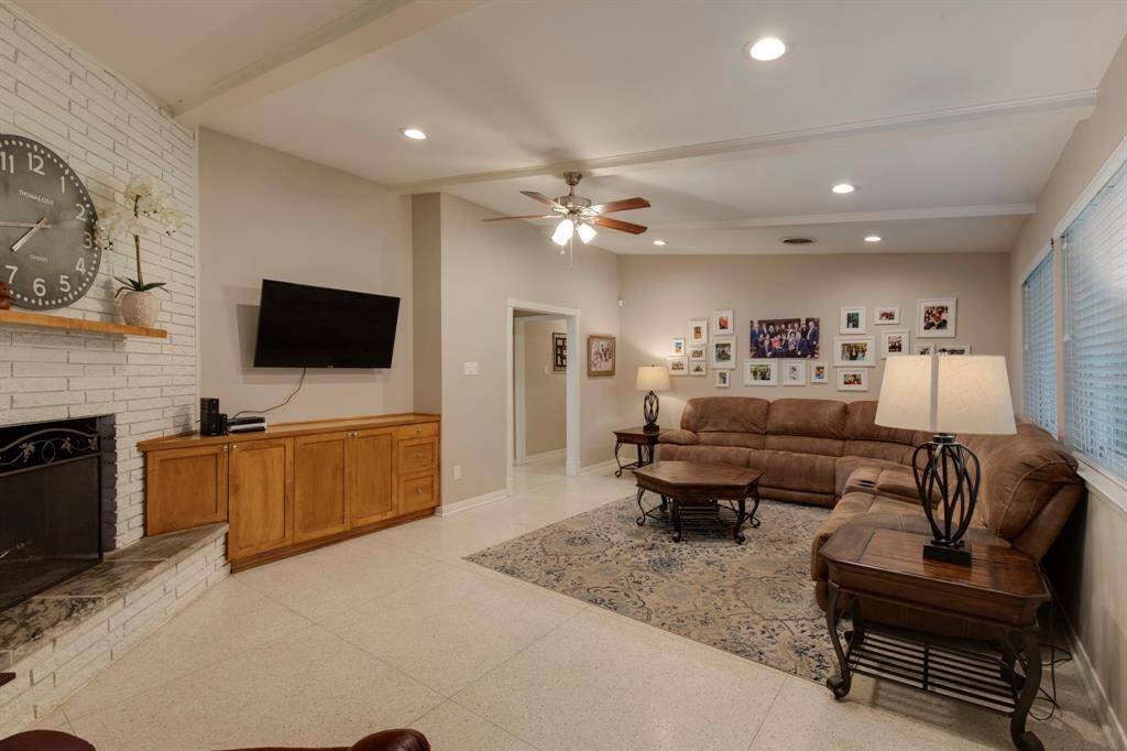 Family room has original Terrazzo floors, raised ceiling with wood beam ceiling treatment, recessed lighting and gas log fireplace with brick surround.
