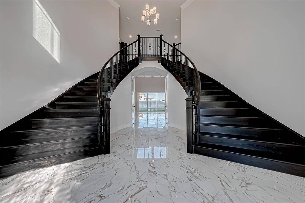 Step into luxury through a dramatic two-story foyer featuring a breathtaking double circular staircase with rich dark wood and wrought iron details. Marble-look tile flooring flows through the main living areas, adding to the elegance.