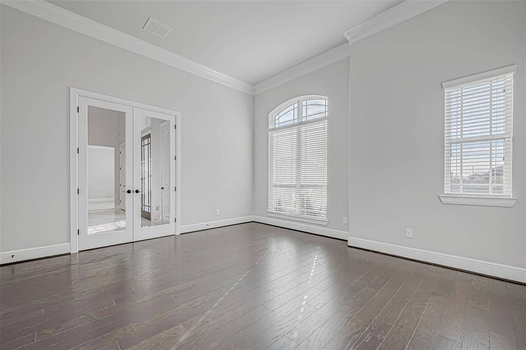 A spacious home office with double glass doors and dark wood flooring sits at the entrance, creating a sophisticated workspace.