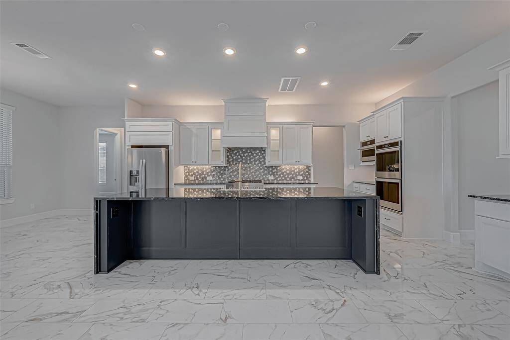 Gourmet KitchenThe bright and stylish kitchen is a chef’s dream. A massive center island with a granite waterfall edge and farmhouse sink anchors the space, surrounded by sleek white cabinetry adorned with gold hardware.
