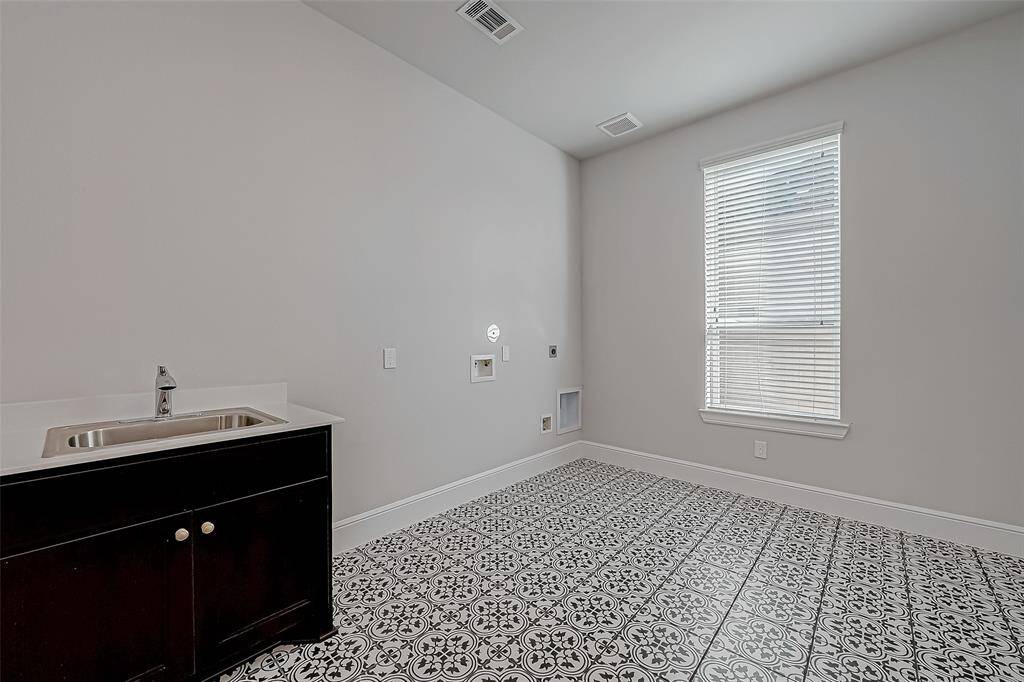 A spacious laundry room featuring stylish black and white decorative tile flooring, a utility sink, and cabinetry for added convenience and storage.