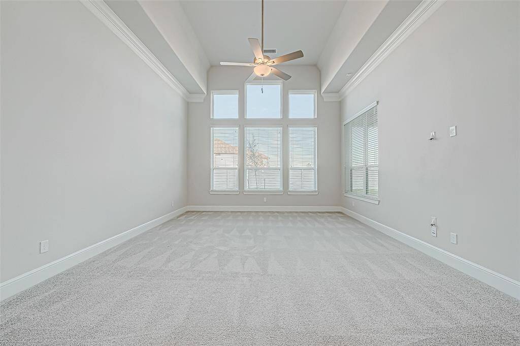The luxurious primary suite is a private sanctuary, accessed through unique double doors. The bedroom features soaring 18-foot tray ceilings, a wall of windows, and a ceiling fan.