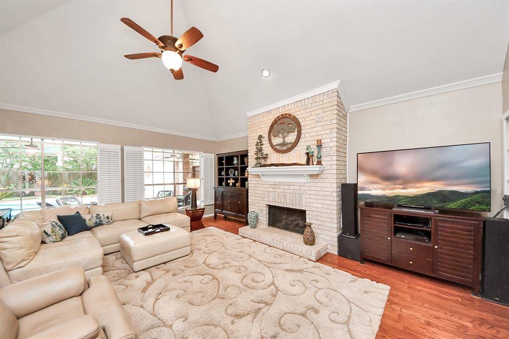 Step into the spacious den featuring soaring ceilings, a striking brick fireplace, and continued wood flooring. Despite its generous size, the space offers a cozy, welcoming atmosphere.